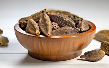 Fresh black cardamom pods displayed in a rustic wooden bowl, highlighting their rich textures.