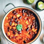 A bright, inviting bowl of vegan chili filled with beans, tomatoes, and topped with avocado slices and cilantro.