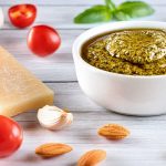 Bowl of Pesto alla Trapanese surrounded by fresh ingredients like tomatoes, almonds, and basil