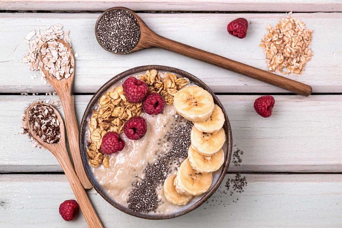 A colorful smoothie bowl with a vibrant pink base, topped with granola, shredded coconut, fresh fruit slices, and chia seeds, photographed on a clean white table with natural lighting.