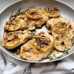A perfectly crispy chicken breast garnished with fresh thyme and lemon slices on a shabby white wooden table.