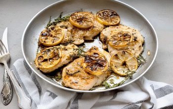 A perfectly crispy chicken breast garnished with fresh thyme and lemon slices on a shabby white wooden table.