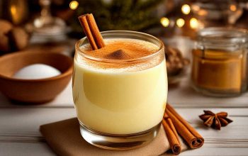 Glass of creamy eggnog on a rustic wooden table with cinnamon sticks and nutmeg