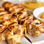 Plated grilled chicken skewers with honey mustard sauce and salad on a rustic plate