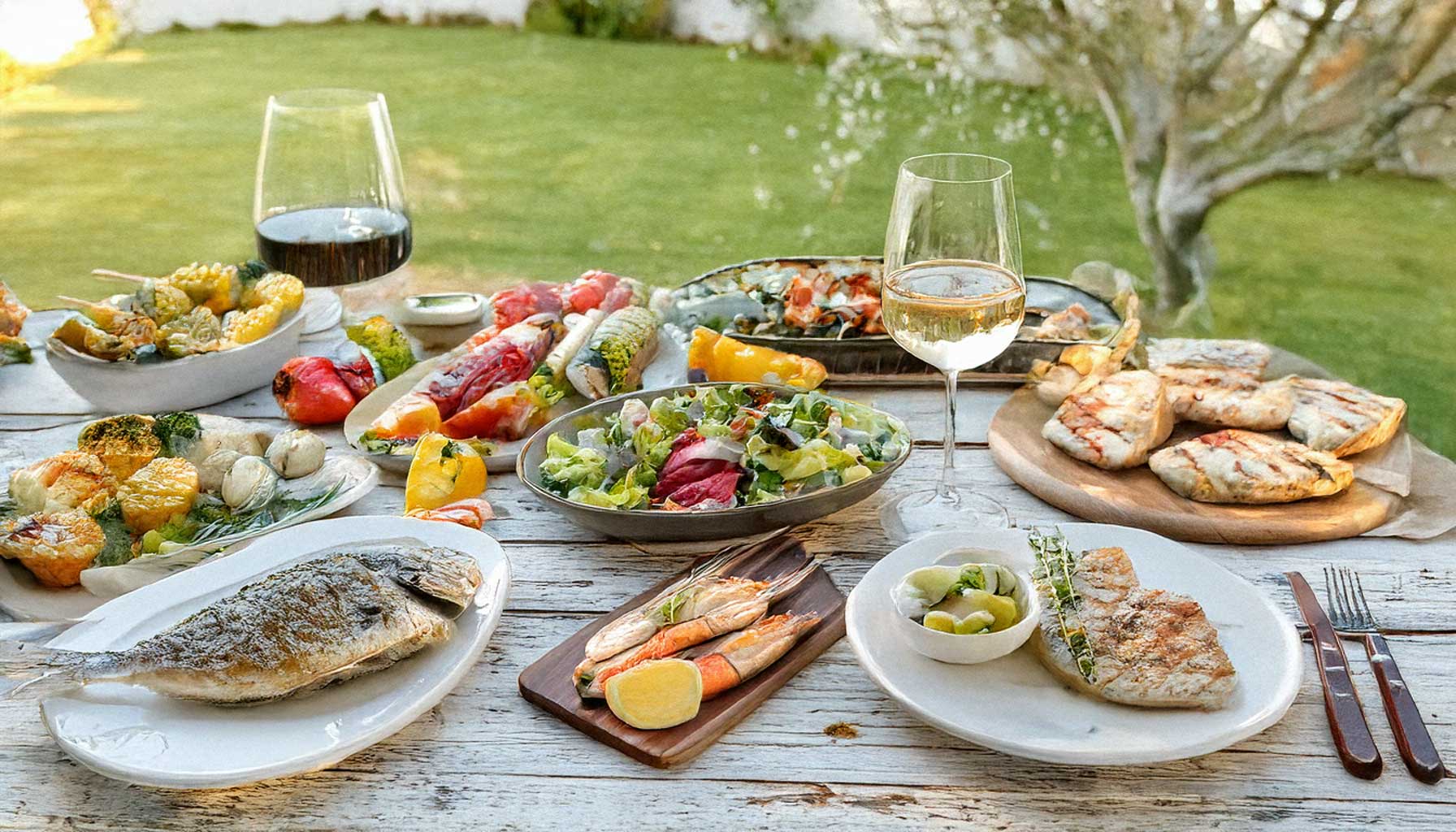 A cozy dinner table with Mediterranean dishes such as hummus, roasted vegetables, pasta, and a glass of red wine, warmly lit and set on a white shabby wooden surface. Title: Mediterranean Diet Lifestyle