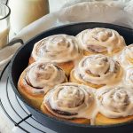 Freshly baked cinnamon rolls with cream cheese frosting on a white wooden table.