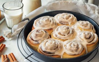 Freshly baked cinnamon rolls with cream cheese frosting on a white wooden table.